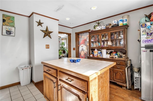 kitchen featuring crown molding, tile counters, a kitchen island, and stainless steel refrigerator