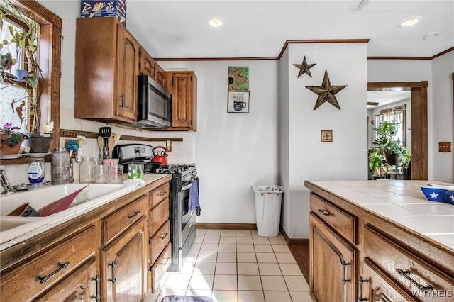 kitchen featuring light tile patterned flooring, appliances with stainless steel finishes, tile counters, crown molding, and a healthy amount of sunlight