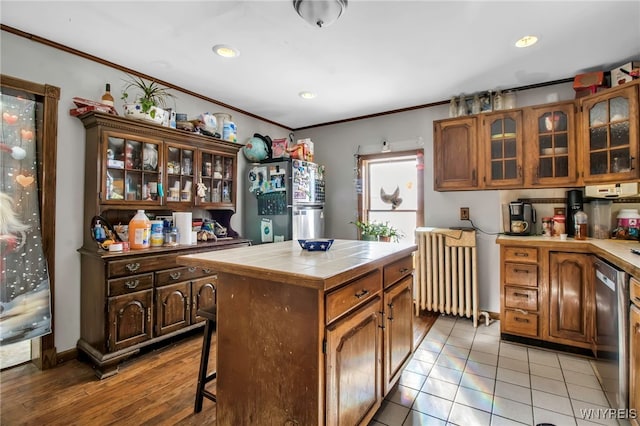 kitchen featuring crown molding, tile countertops, a center island, appliances with stainless steel finishes, and radiator heating unit