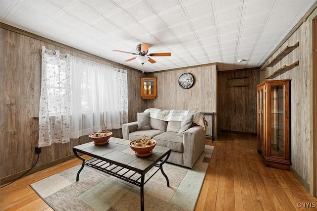 living room with hardwood / wood-style flooring, ceiling fan, and wood walls