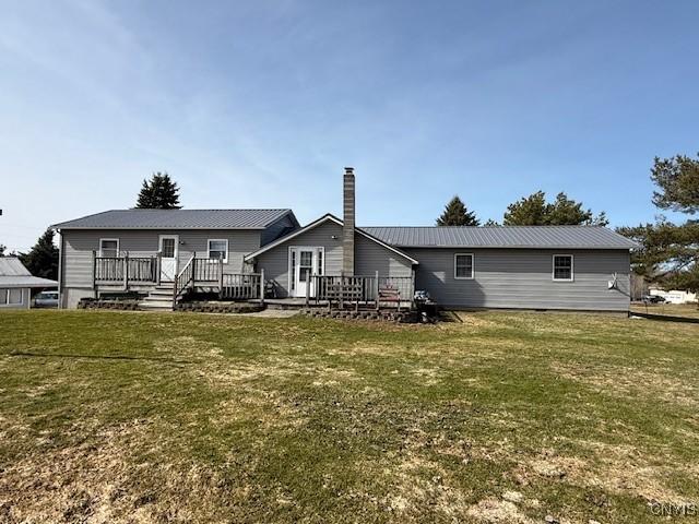 back of property featuring a lawn, a chimney, a wooden deck, and metal roof