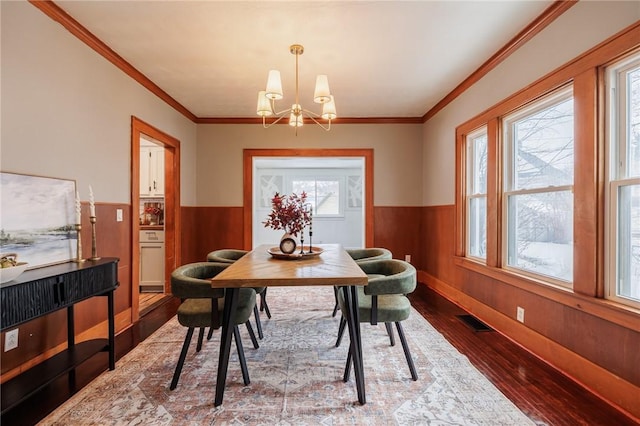 dining room featuring wood-type flooring, crown molding, wooden walls, and an inviting chandelier