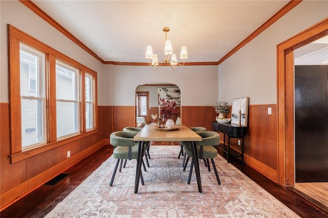 dining area featuring an inviting chandelier, wood-type flooring, crown molding, and wood walls