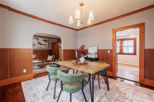 dining area featuring wood-type flooring, ornamental molding, a chandelier, and wood walls