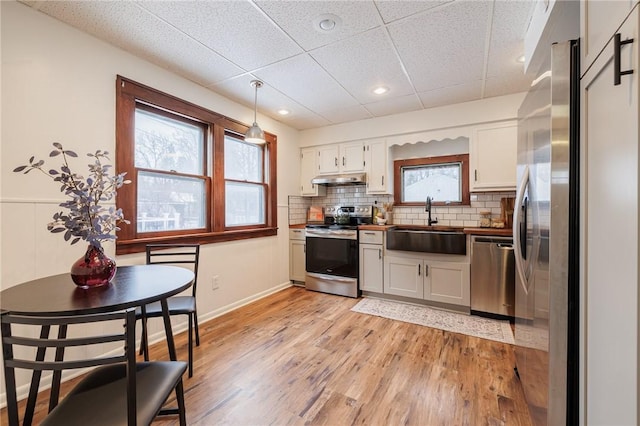 kitchen with sink, decorative light fixtures, light hardwood / wood-style flooring, stainless steel appliances, and white cabinets