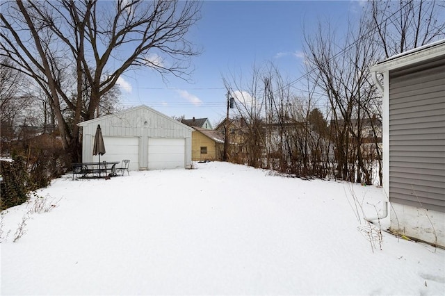 yard covered in snow featuring a garage and an outbuilding