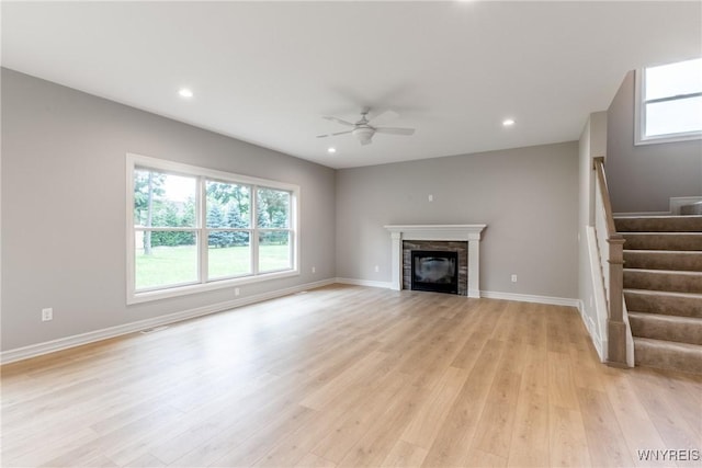 unfurnished living room with ceiling fan, a fireplace, and light wood-type flooring