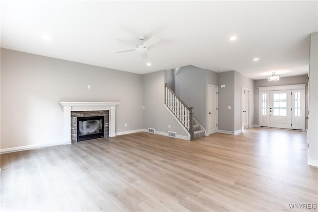 unfurnished living room with ceiling fan, a stone fireplace, and light wood-type flooring