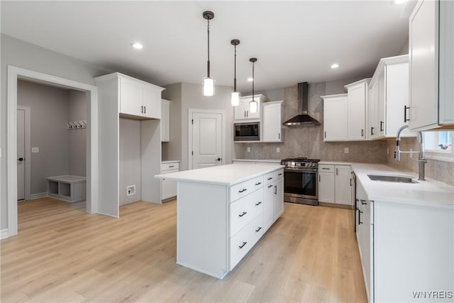 kitchen featuring sink, appliances with stainless steel finishes, a kitchen island, wall chimney range hood, and white cabinets