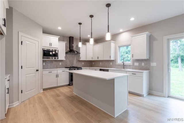 kitchen with white cabinets, appliances with stainless steel finishes, and wall chimney range hood