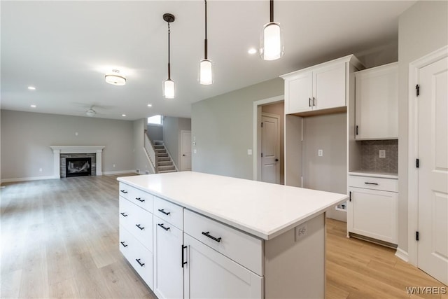 kitchen featuring a kitchen island, pendant lighting, a fireplace, white cabinetry, and light hardwood / wood-style floors