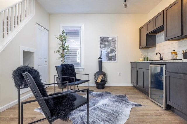 interior space featuring decorative backsplash, dark brown cabinets, beverage cooler, and light hardwood / wood-style flooring