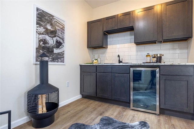 bar with beverage cooler, sink, decorative backsplash, and light hardwood / wood-style flooring