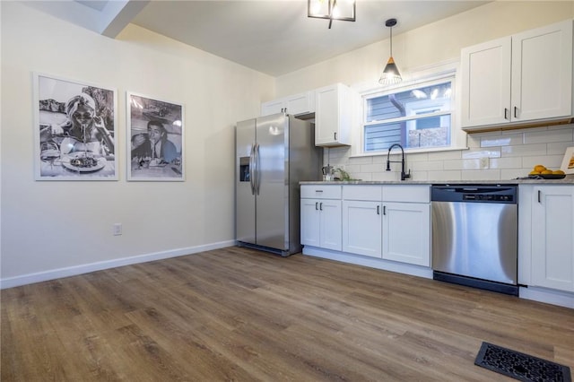 kitchen featuring appliances with stainless steel finishes, white cabinetry, backsplash, hanging light fixtures, and hardwood / wood-style flooring