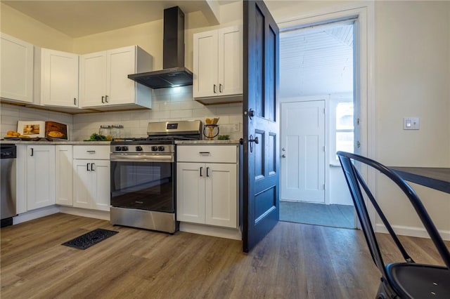 kitchen with wood-type flooring, appliances with stainless steel finishes, white cabinets, and wall chimney exhaust hood