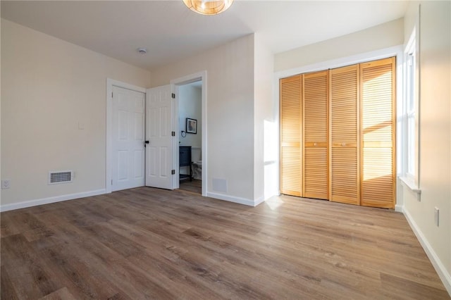 unfurnished bedroom with ensuite bathroom, hardwood / wood-style floors, and a closet