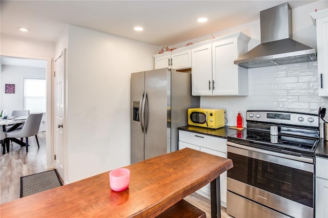 kitchen featuring white cabinets, decorative backsplash, light hardwood / wood-style floors, stainless steel appliances, and wall chimney range hood