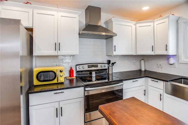 kitchen featuring wall chimney exhaust hood, white cabinetry, dark stone countertops, stainless steel appliances, and decorative backsplash