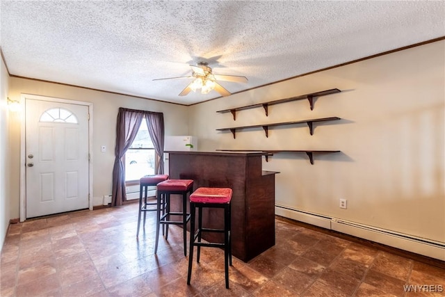 dining room with ceiling fan, baseboard heating, ornamental molding, a textured ceiling, and bar area