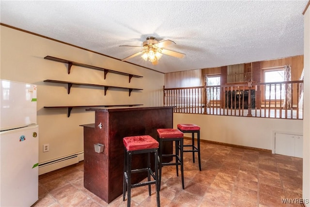 bar with white refrigerator, ceiling fan, a textured ceiling, and a baseboard heating unit