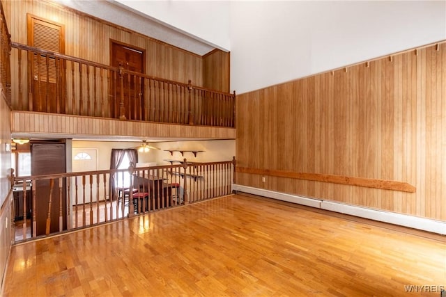 spare room with wood-type flooring, wooden walls, a baseboard radiator, and a high ceiling