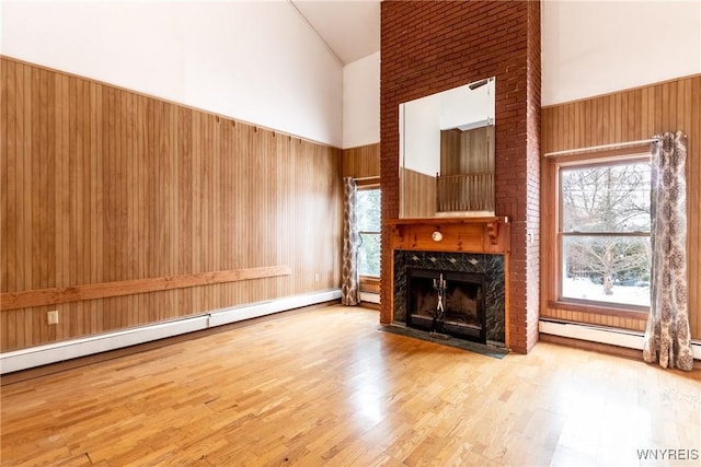 unfurnished living room featuring light hardwood / wood-style flooring, baseboard heating, high vaulted ceiling, a high end fireplace, and wood walls