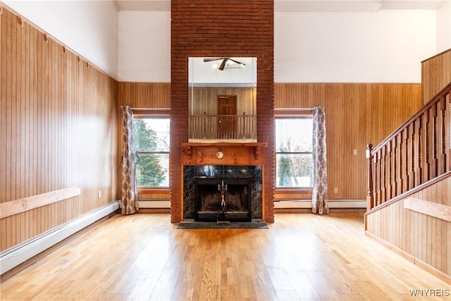 unfurnished living room featuring a premium fireplace, a high ceiling, wood-type flooring, a baseboard radiator, and wood walls