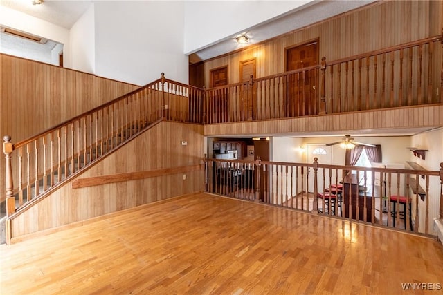 unfurnished living room featuring a high ceiling, hardwood / wood-style floors, ceiling fan, and wood walls