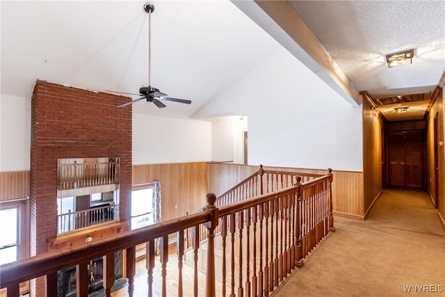 hallway with light colored carpet, wooden walls, vaulted ceiling, and a textured ceiling