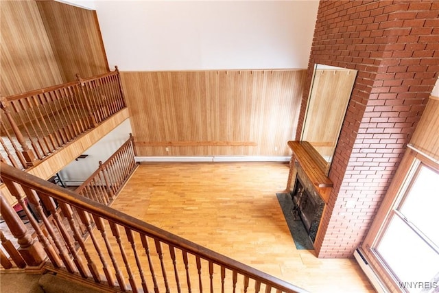 interior space with a towering ceiling, wooden walls, a baseboard heating unit, a brick fireplace, and light wood-type flooring