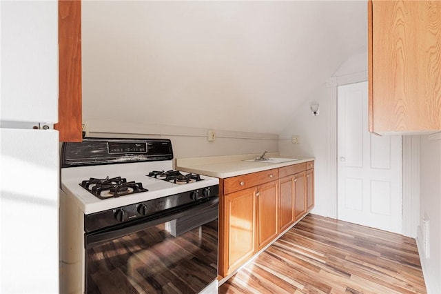 kitchen with gas range, vaulted ceiling, sink, and light hardwood / wood-style floors