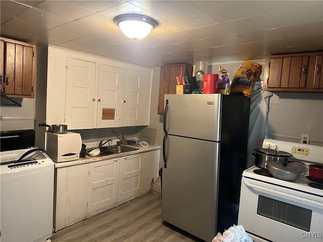 kitchen with washer / dryer, sink, light wood-type flooring, stainless steel refrigerator, and electric stove