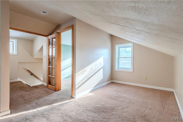 additional living space featuring a textured ceiling, light carpet, and vaulted ceiling