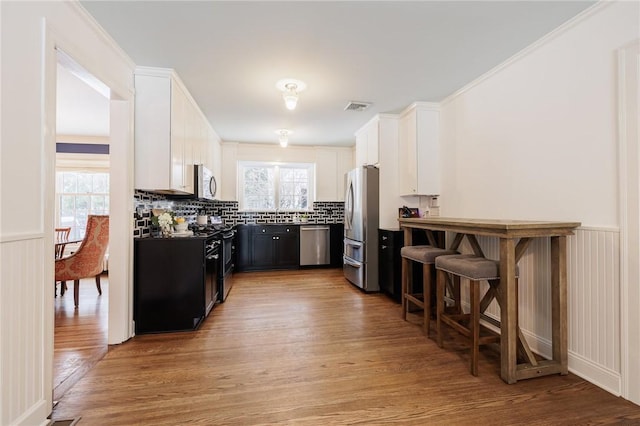 kitchen featuring backsplash, a kitchen bar, white cabinets, stainless steel appliances, and light wood-type flooring