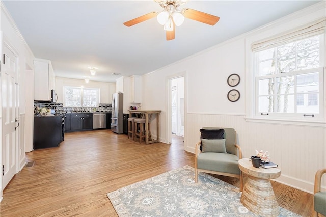 living room with ornamental molding, ceiling fan, and light hardwood / wood-style floors