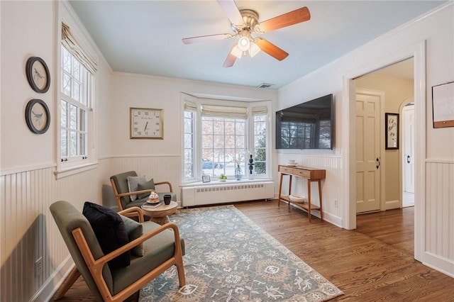 living area featuring hardwood / wood-style flooring, crown molding, radiator, and ceiling fan