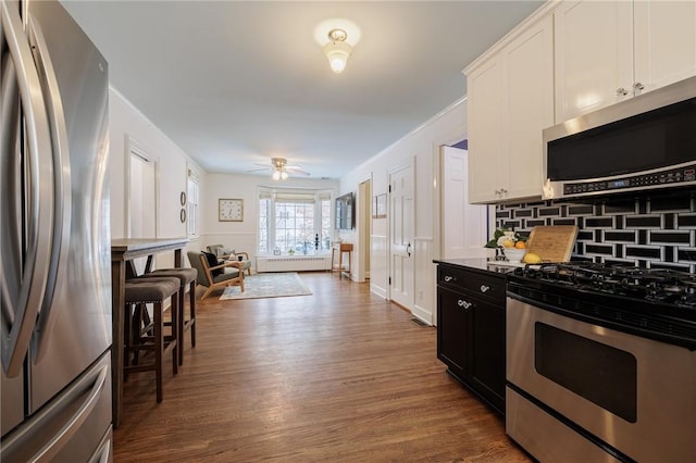 kitchen with dark wood-type flooring, crown molding, appliances with stainless steel finishes, white cabinets, and backsplash