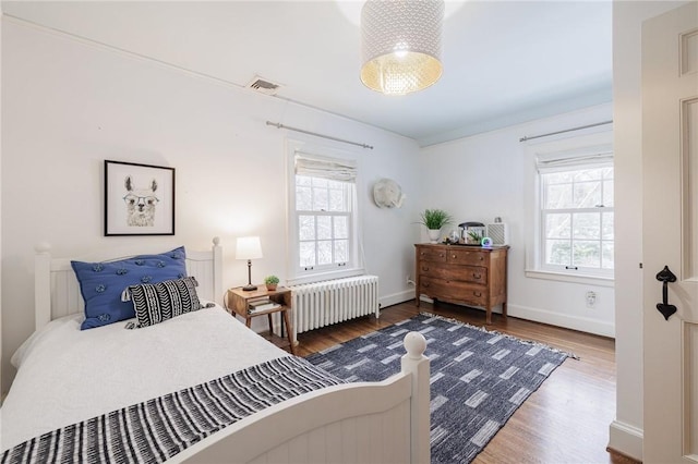 bedroom featuring multiple windows, wood-type flooring, and radiator