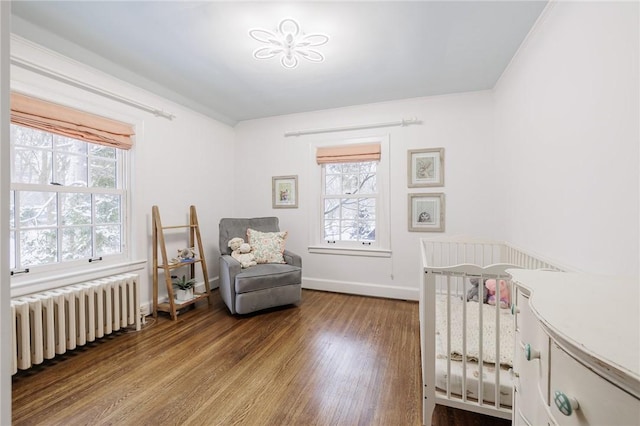 bedroom featuring hardwood / wood-style flooring, a nursery area, radiator, and multiple windows