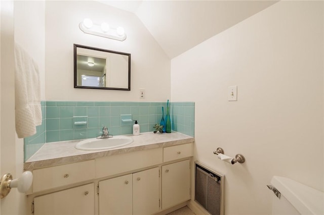 bathroom featuring lofted ceiling, vanity, decorative backsplash, and toilet