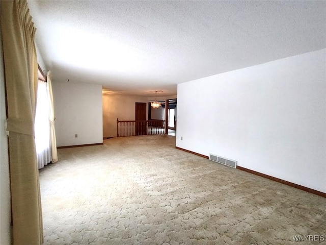 carpeted spare room featuring an inviting chandelier and a textured ceiling