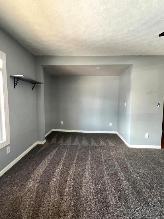 empty room featuring a healthy amount of sunlight, a textured ceiling, and dark colored carpet