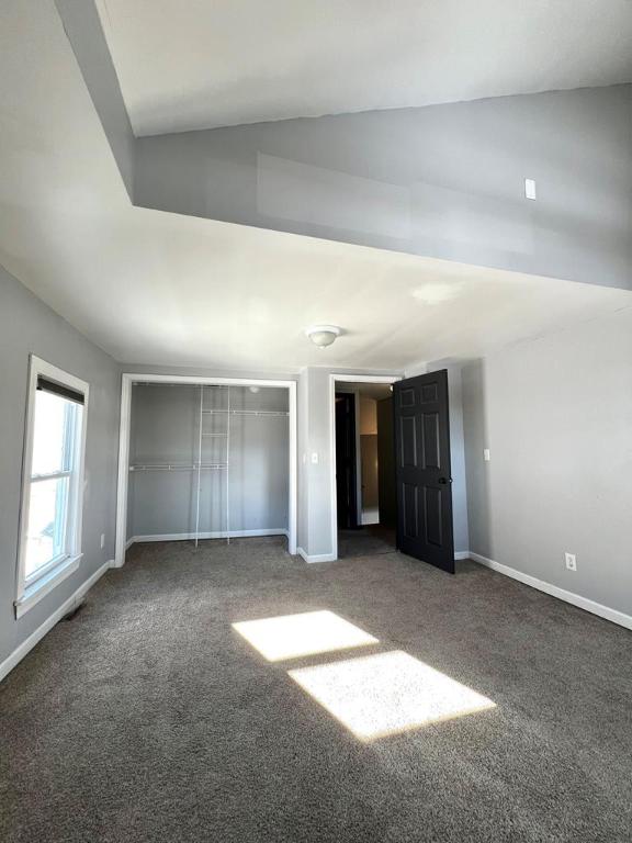 unfurnished bedroom with lofted ceiling and dark carpet