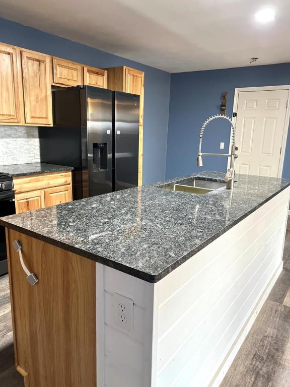 kitchen with range, dark stone counters, stainless steel fridge, and a center island with sink