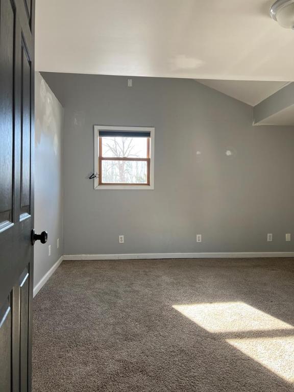 unfurnished room with dark carpet and vaulted ceiling