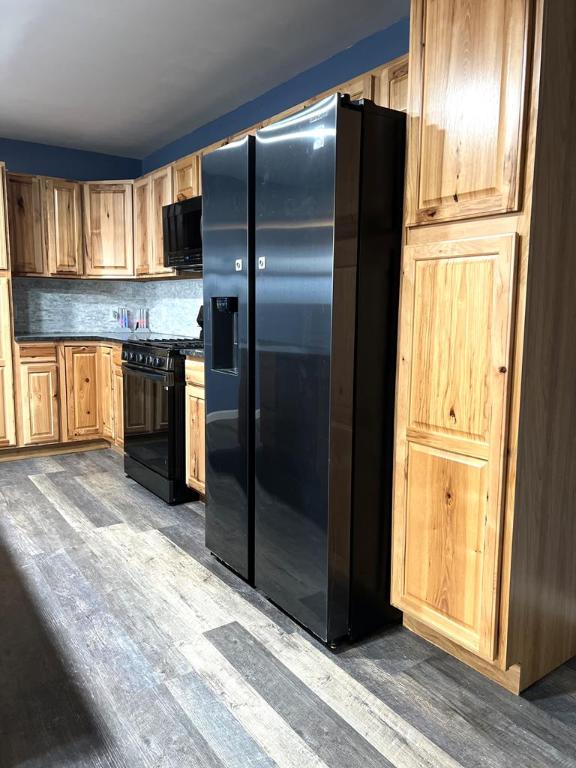 kitchen with dark wood-type flooring, decorative backsplash, and black appliances