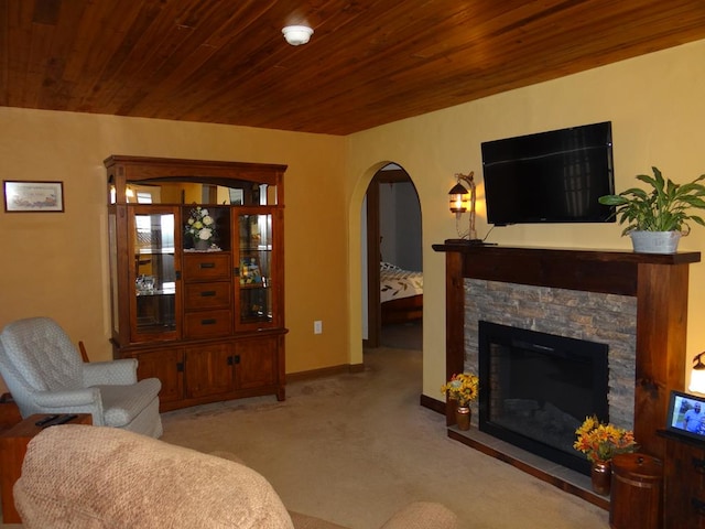 carpeted living room featuring a stone fireplace and wood ceiling