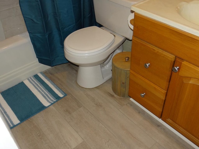 full bathroom featuring hardwood / wood-style flooring, shower / bathtub combination with curtain, vanity, and toilet