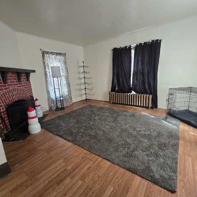 living room with radiator, hardwood / wood-style floors, and a brick fireplace