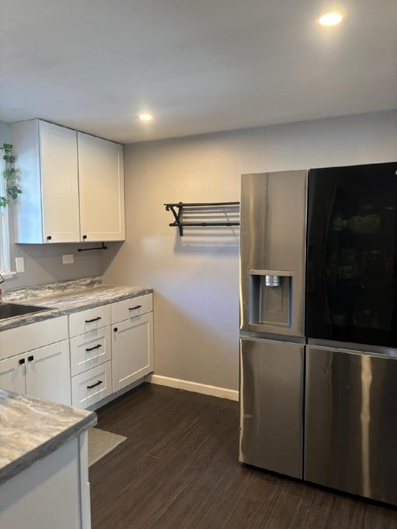 kitchen featuring stainless steel refrigerator with ice dispenser, dark wood-type flooring, sink, white cabinetry, and light stone counters